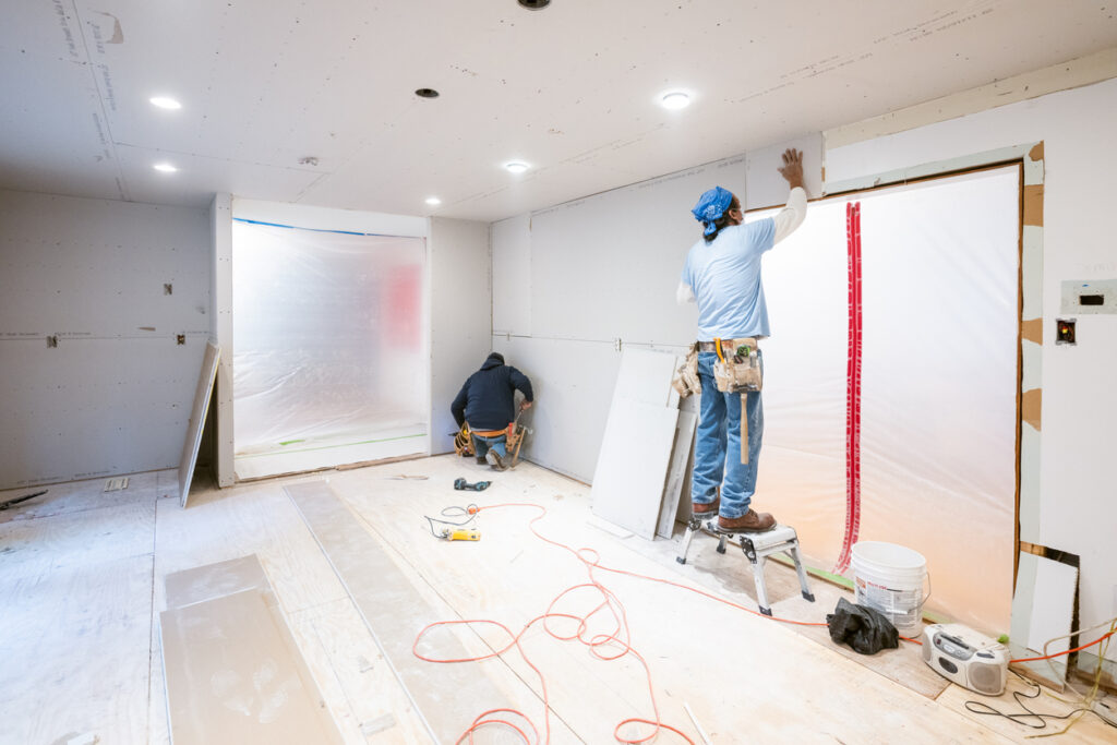 Workers installing drywall in a basement during refinishing project
